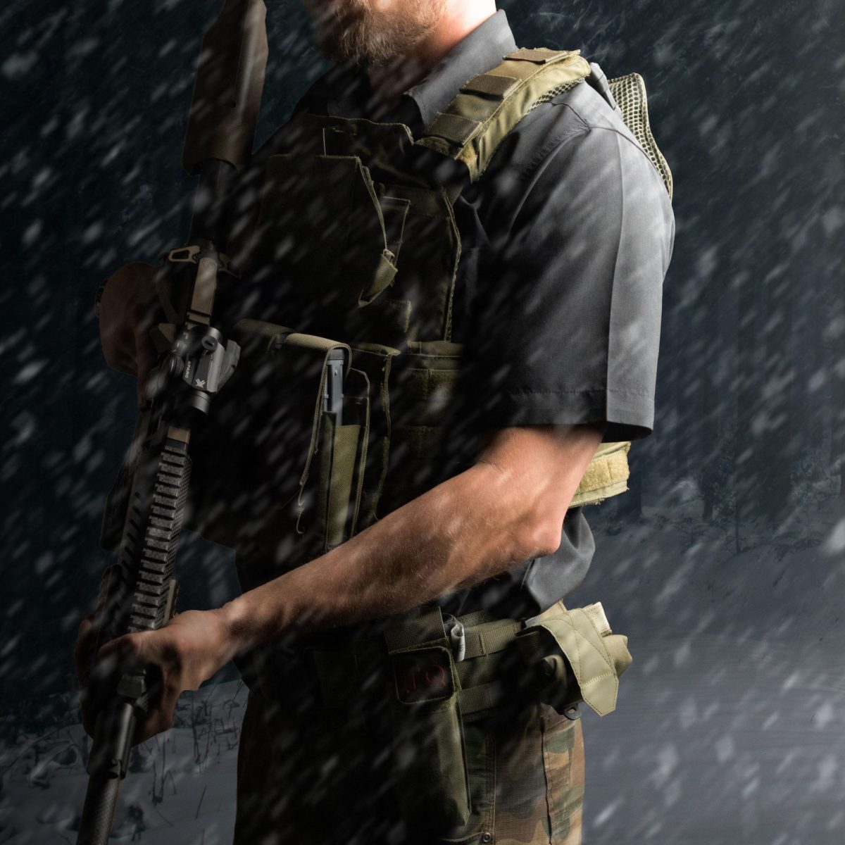 A tactical operator wearing an olive drab plate carrier and battle belt, holding a rifle in a snowy environment, showcasing cold-weather readiness and combat gear.